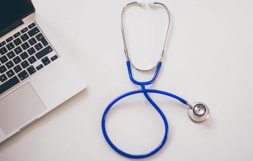 blue stethoscope on table next to laptop