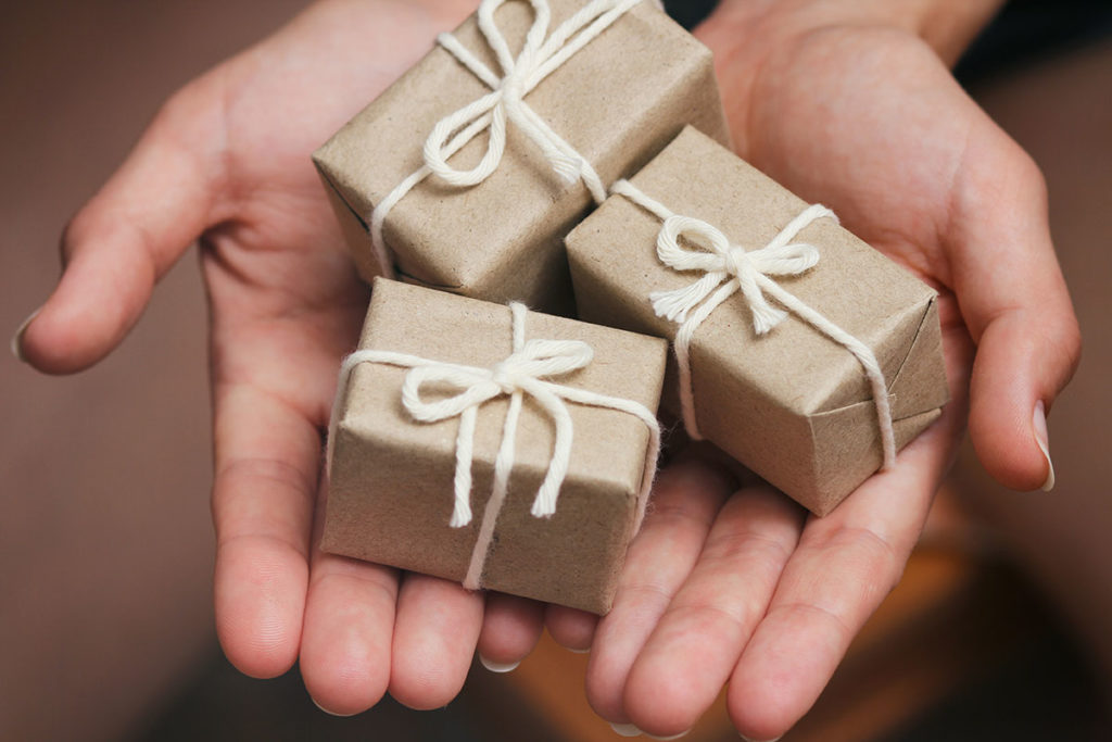 Three small packages wrapped in brown paper in the palm of someone's hands to represent planned giving